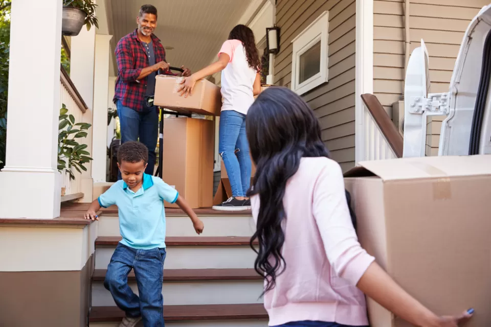 A family of Black Americans brings moving boxes into a home.